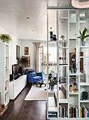 Floor-to-ceiling bookcase as partition with view of blue leather armchair in front of open balcony door