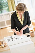Frau zeichnet asiatische Schriftzeichen auf Papierrolle