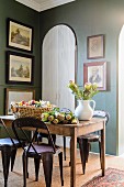 Flowers on rustic wooden table and retro-style metal chairs in corner of traditional dining room with framed pictures on green walls