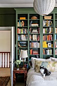 Katze auf Bett vor grünem Bücherregal neben offener Tür