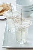 Lacy paper doilies pierced by straws on drinking glasses: as decoration and to keep out insects