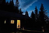 Alpine cabin at dusk with light pouring through open door