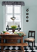 Vegetables on Biedermeier table, old hunting horn and collection of small hunting trophies in kitchen-dining room; seat of chair upholstered with old flour sack