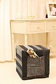 Square pouffe with hand-sewn, denim cover in front of rustic, white-painted console table with drawers