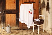 Table cloth with embroidered floral motif hanging over washing line and laundry basket on chair in rustic interior
