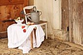Table cloth embroidered with floral motif on wooden trestle in front of watering can on kitchen chair in rustic interior