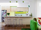 Kitchen with spring green accents and Ghost stools at kitchen counter; green sofa in foreground