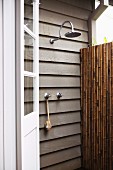 Outdoor shower on wooden wall of house; partially visible bamboo screen