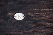 Number 8 on small, old metal plate on dark, weathered wood