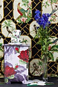 Tassenstapel auf Kästchen mit Blumenmotiven vor tapezierter Wand mit Vogelbildern