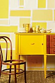 Wall design in stylised stone effect behind yellow-painted vintage cabinet and Thonet chair missing its rush seat