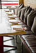 Leather bench with row of cushions at wooden table set with water glasses and red and white napkins