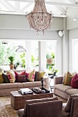 Sofa set with colourful scatter cushions around wicker coffee table and chandelier hanging amongst exposed roof structure in elegant living room