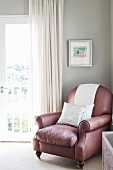 Leather armchair in corner of room against pale grey wall next to window with floor-length curtain