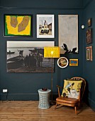 Small, vintage armchair next to standard lamp with yellow lampshade below gallery of pictures on wall painted blue-grey