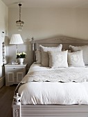 Elegant bed linen on pale grey antique bed with headboard next to bedside table and table lamp in rustic ambiance