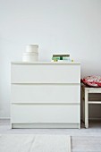 Set of storage boxes on simple, white chest of drawers against wall