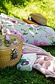 Floral cushions, straw hat, blanket, book and picnic basket on lawn