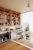 Table made from wooden boards of different lengths in modern kitchen opposite wooden shelves above stainless steel kitchen counter
