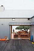 South African beach house with sheet metal facade - view from deck through open interior to seating area on beach with large tree canopy