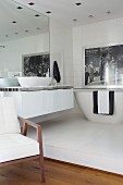 Modern ensuite bathroom with large mirror, washstand and bathtub on white platform