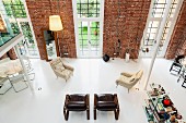 View from gallery into loft apartment with widely spaced armchairs and designer standard lamps against brick wall with floor-to-ceiling windows