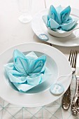 Decorative place settings with lotus flower napkins and hand-crafted, modelling clay pendants with initials as name cards for guests