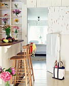 Esstheke mit rustikalen Barhockern vor Wand mit Blumenvasen im Regal und offener Schlafzimmertür