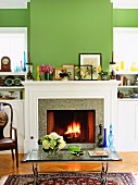 Grün getöntes Wohnzimmer mit Glastisch vor offenem Kamin und Feuer
