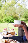Woman sitting garden with cup of tea & pastries on cake stand