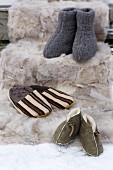 Verschiedene Hausschuhe (gestrickt, Lammfell und Fellpantoffeln) auf einer Pelzdecke im Schnee