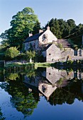 Kleiner See mit perfekter Spiegelung des dahinterliegenden englischen Landhauses mit Natursteinfassade