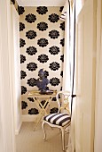 Blick durch offene Tür auf postmodernen Stuhl mit gestreiftem Bezug und Beistelltisch vor tapezierter Wand mit schwarz-weißem Blumenmuster
