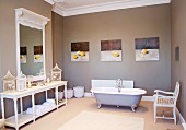Freistehende Vintage Badewanne vor Bildergalerie und Vogelkäfige auf halbhohem Regal vor Wandspiegel in grau getöntem Badezimmer mit traditionellem Flair