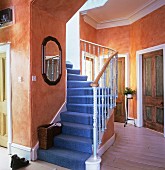 Traditionelles Treppenhaus mit orange gelb getönten Wänden und blauer Teppichbelag auf Treppe