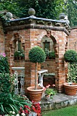 Gemauerter Gartenpavillon aus Ziegel mit fensterartigen Öffnungen und Bäumchen im Terrakottatopf auf Podest