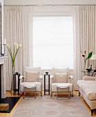 Modernes cremefarbenes Wohnzimmer mit Kamin, Sitzecke mit Stühlen & Sofa am Fenster mit bodenlangen Vorhängen