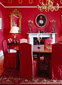 Esszimmer in Rot mit Kamin, ovalem Tisch, Stühlen mit Hussen, Kerzenleuchtern & Kronleuchter