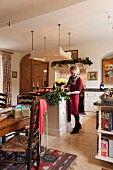 Dining area with wrapped presents in front of woman standing at free-standing counter below suspended, overhead lighting unit in open-plan, country-house kitchen