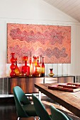 Indigenous Australian artwork above collection of artistic glass bottles (Blenko) on 50s sideboard and classic Executive chairs (Saarinen) around dining table in foreground