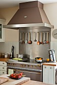 Modern electric cooker with retro elements and cooking utensils hanging from bar below extractor hood