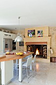 Open fireplace with integrated firewood storage in kitchen-dining room with industrial-style pendant lamps above counter-height table