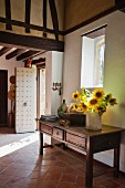 Vase of sunflowers on wooden console table in foyer of country house with terracotta floor