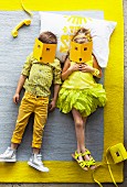 Children dressed in shades of yellow lying on grey rug with yellow border