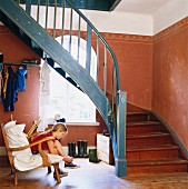 Mädchen bindet sich die Schuhe zu im Hauseingang mit Holztreppe in altem Landhaus