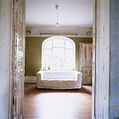 Blick durch offene Tür auf Sofa mit weisser Husse am Fenster mit Rundbogen in Vintage Ambiente