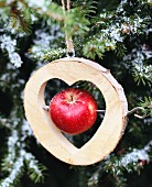Holzscheibe mit ausgeschnittener Herzform und aufgespiesstem Apfel vor Weihnachtsbaum