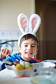 Boy wearing bunny ears painting Easter eggs