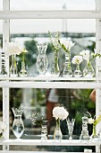 Schmales Holzregal am Fenster mit Glasvasen und weissen Blumen
