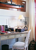 Chair and simple console table with table lamp against half-height wood panelling and model ship on wall